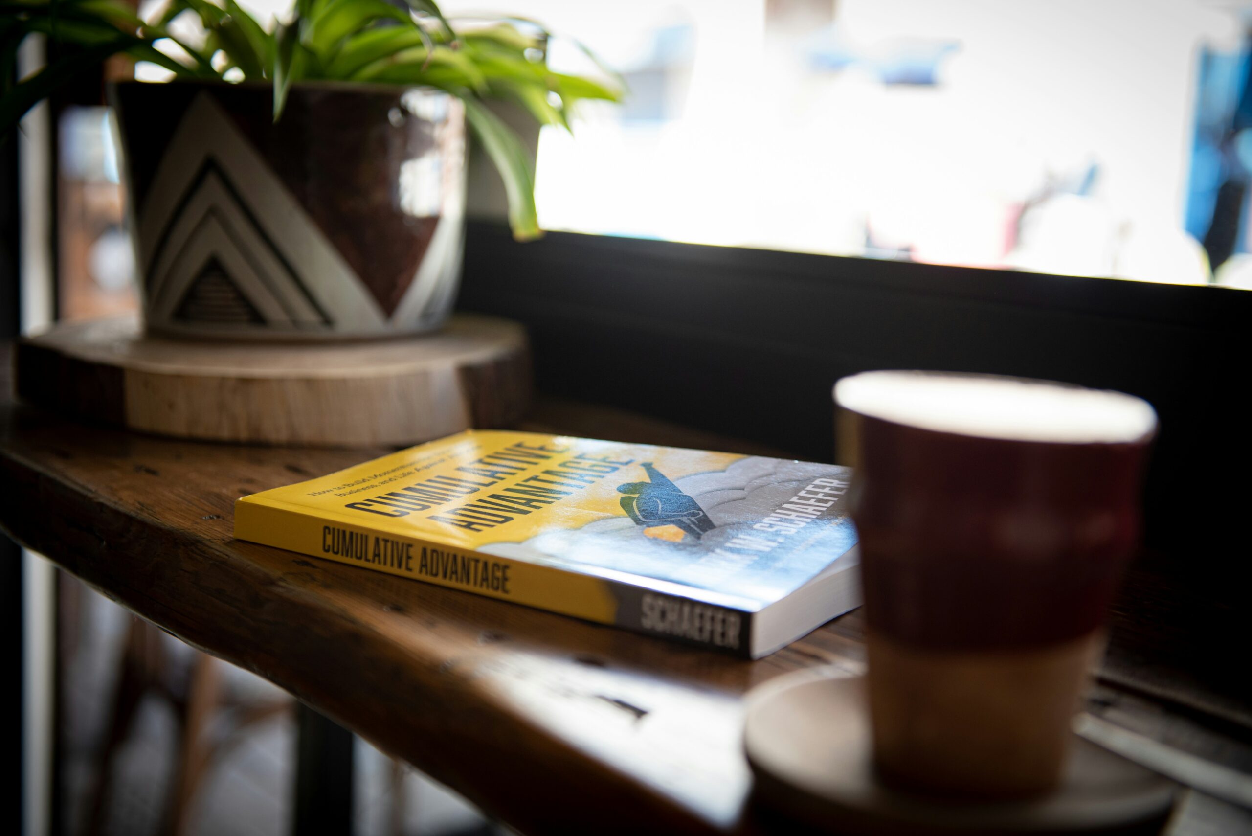 blue and yellow book beside brown ceramic mug on brown wooden table